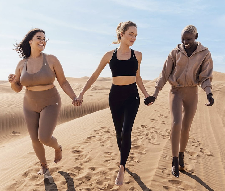 Tre ragazze in top e leggings che corrono sulla spiaggia