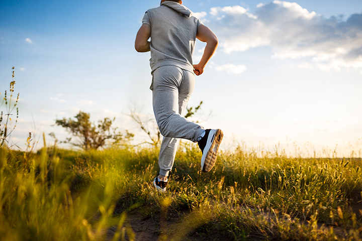 Uomo di schiena in tutta da ginnastica che corre al tramonto su un prato